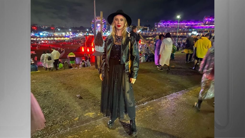 Jovem loira de chapéu preto posando com cenário do festival