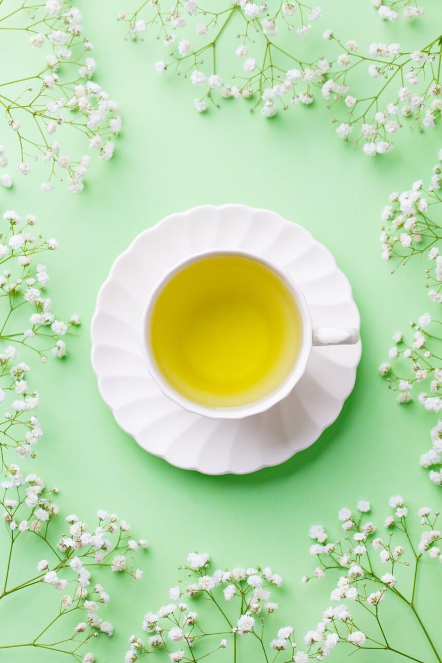 Green tea in a white cup with gypsophila flowers on green pastel background. Top view.